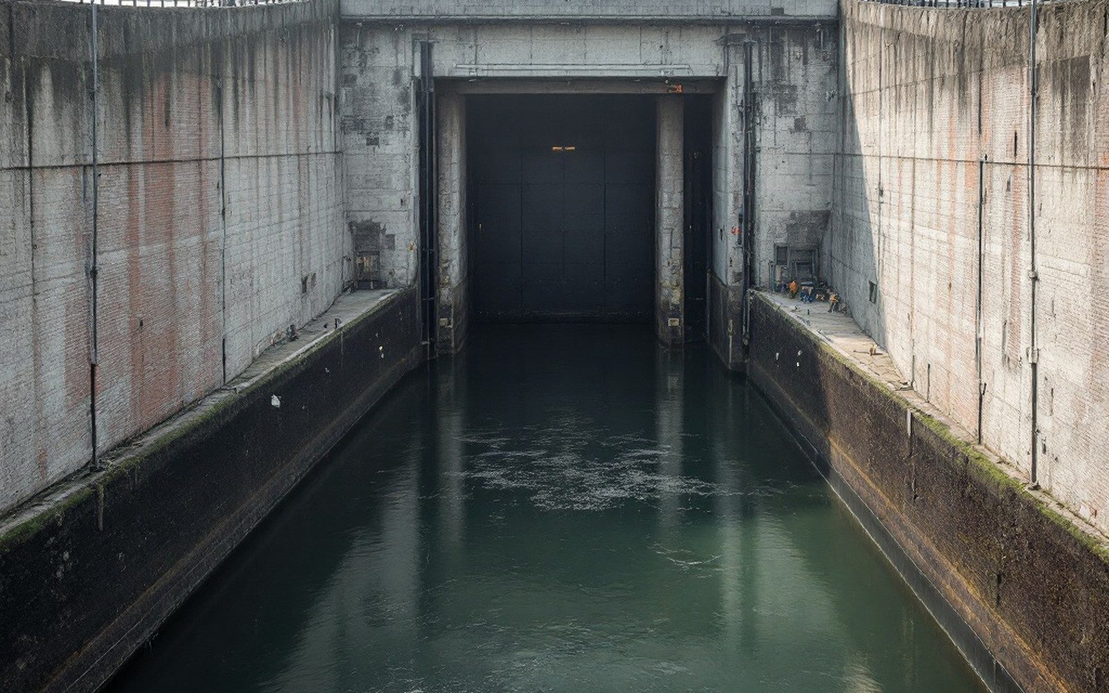A river lock chamber with its gates closed and concrete walls streaked, no vessel