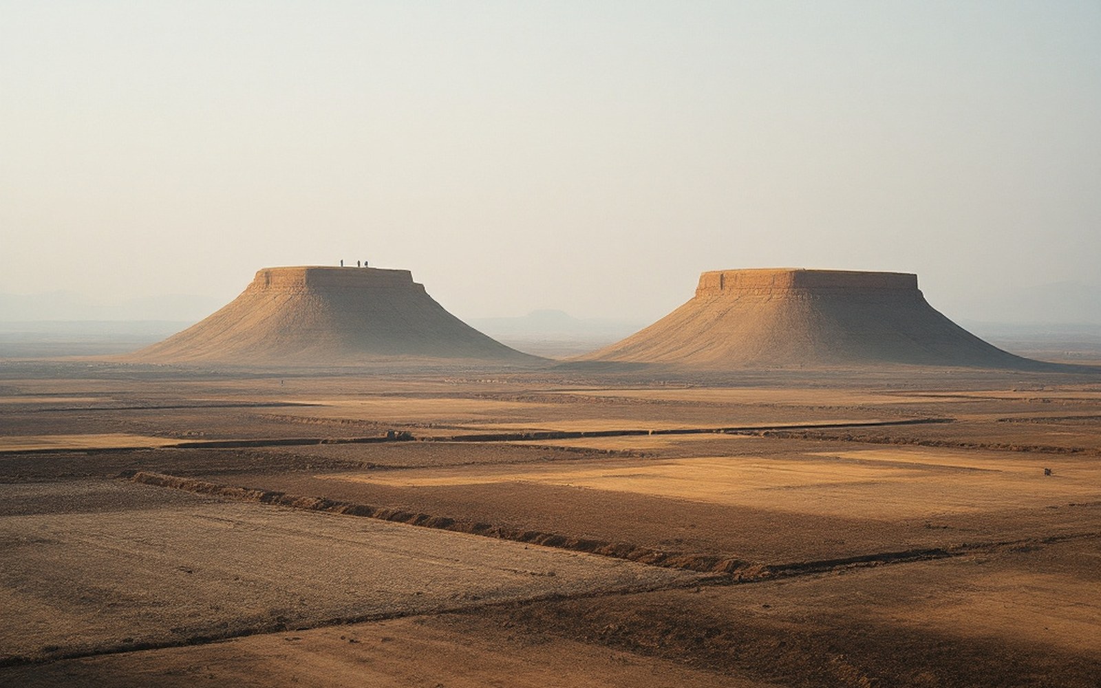 Two flat-topped hills of similar height standing separately above cleared land, hazy afternoon light